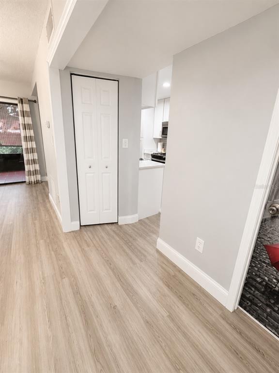 A view of a hallway with light wood flooring, a white bi-fold closet, and a kitchen — 5979 WINDHOVER DRIVE UNIT 7A, ORLANDO, FL