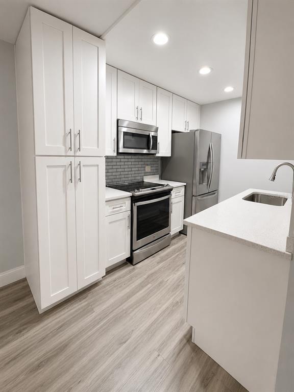 A kitchen features white cabinets, stainless steel appliances, a gray subway tile backsplash, and light flooring — 5979 WINDHOVER DRIVE UNIT 7A, ORLANDO, FL