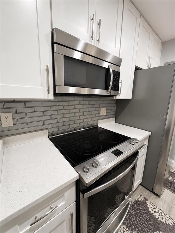 A kitchen features white cabinets, stainless steel appliances, a glass stovetop, and gray subway tile — 5979 WINDHOVER DRIVE UNIT 7A, ORLANDO, FL