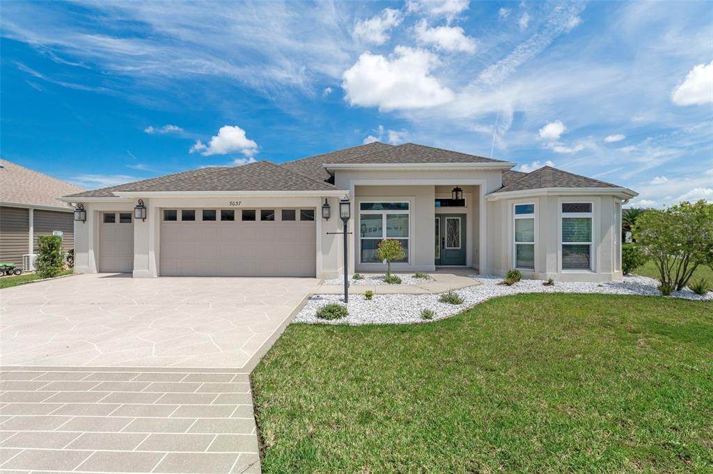A single-story beige house with a two-car garage and a landscaped front yard — 3037 LICCIARDELLO PATH, THE VILLAGES, FL