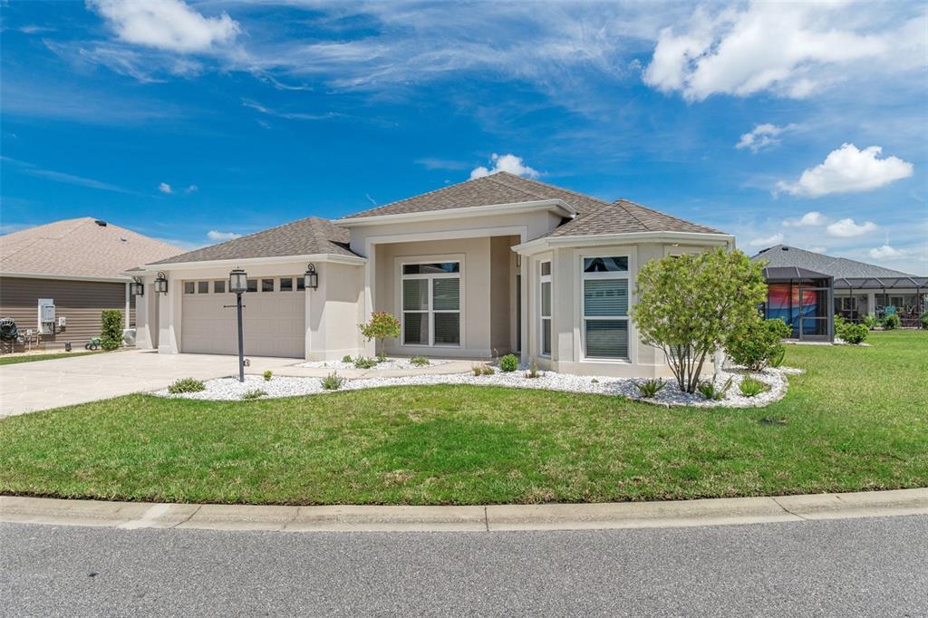 The exterior of a single-story house features a gray front door, white stucco, and gravel — 3037 LICCIARDELLO PATH, THE VILLAGES, FL