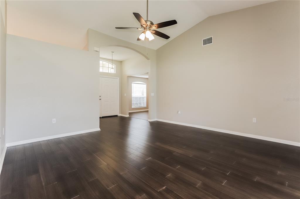 An empty living room features dark wood flooring, a vaulted ceiling, and a ceiling fan — 3407 IMPERIAL MANOR WAY, MULBERRY, FL