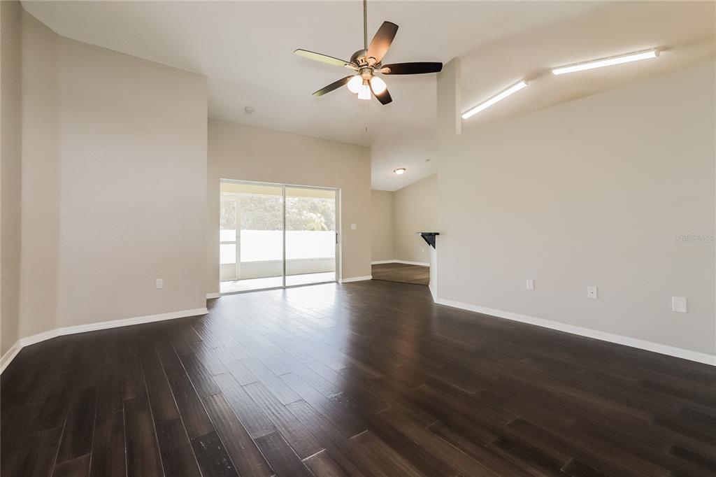 A spacious living room with dark wood flooring, a ceiling fan, and sliding glass doors — 3407 IMPERIAL MANOR WAY, MULBERRY, FL
