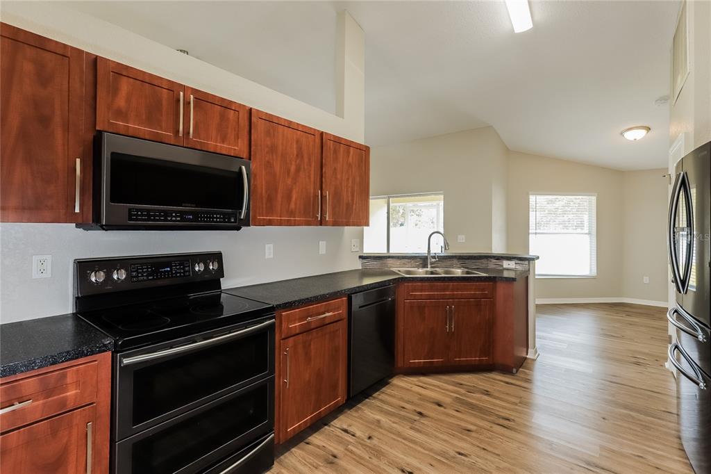 A kitchen with wood cabinets, black appliances, and dark countertops overlooks an open living area — 3407 IMPERIAL MANOR WAY, MULBERRY, FL