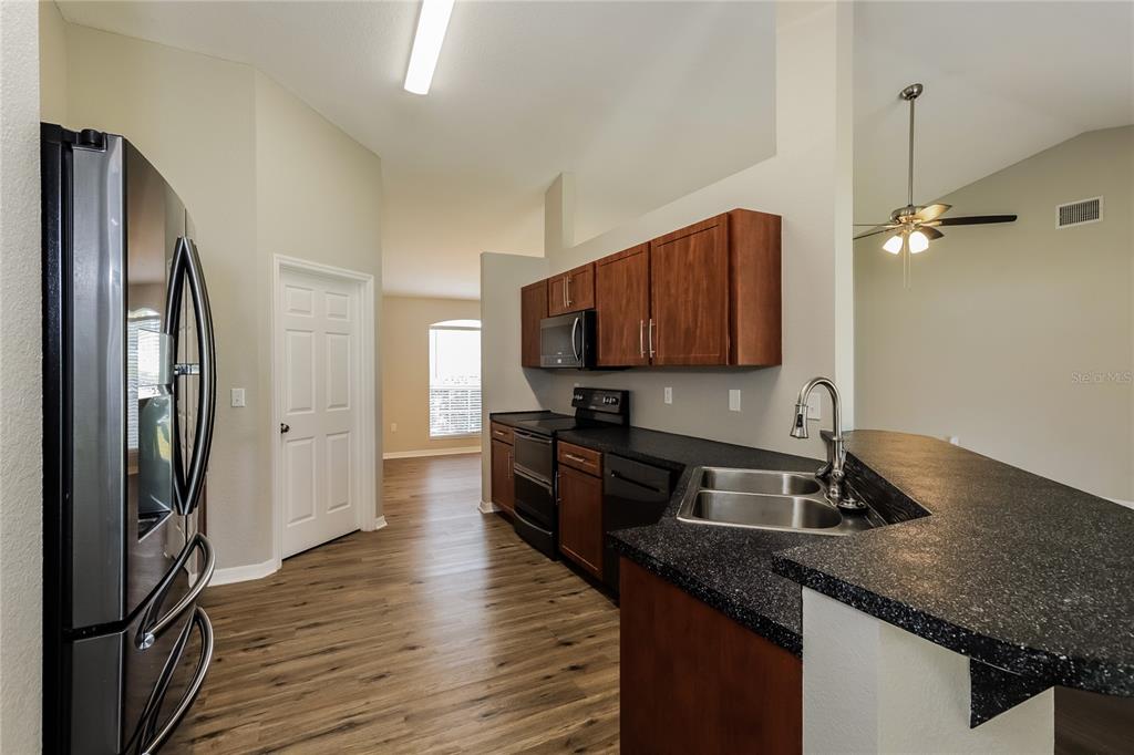 A kitchen features dark wood cabinets, black countertops, stainless steel appliances, and wood-look flooring — 3407 IMPERIAL MANOR WAY, MULBERRY, FL