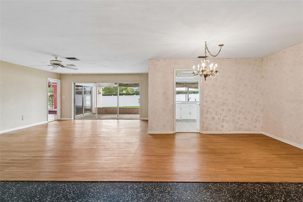 An open-concept living and dining area features wood-look flooring, a chandelier, and a kitchen doorway — 14363 NEPTUNE ROAD, SEMINOLE, FL