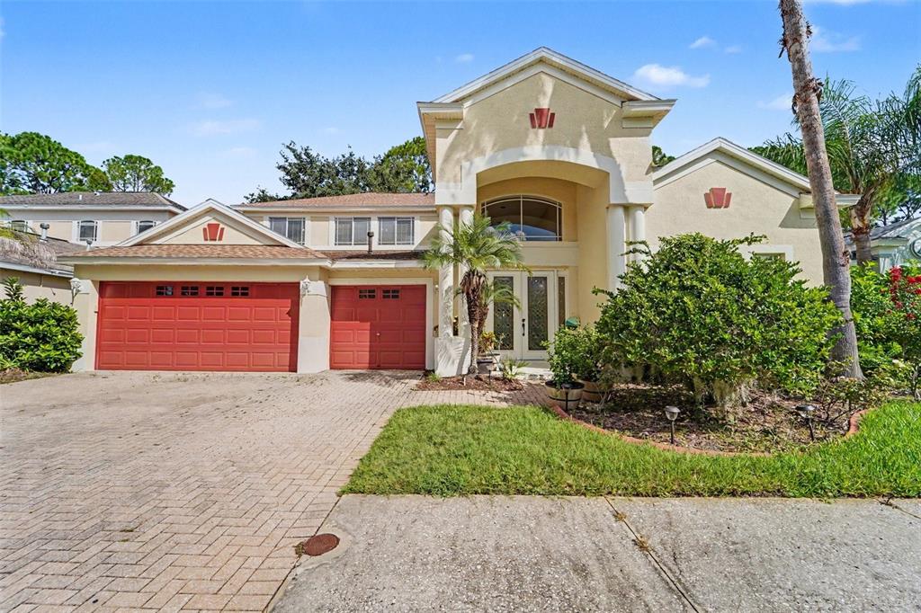 A two-story house with a red three-car garage, light stucco exterior, and a paved driveway — 10409 CANARY ISLE DRIVE, TAMPA, FL