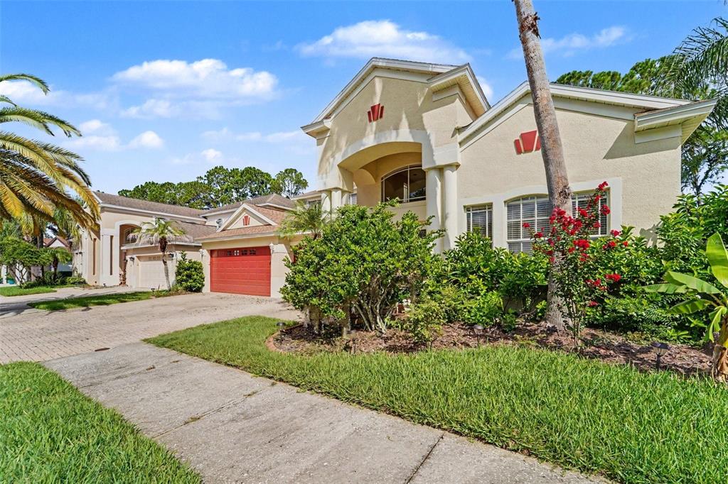 A two-story stucco house with a red garage door and a landscaped front yard — 10409 CANARY ISLE DRIVE, TAMPA, FL