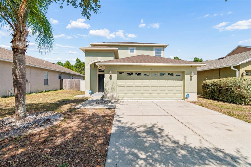 A two-story house with a light green exterior, a two-car garage, and a palm tree — 915 WINDTON OAK DRIVE, RUSKIN, FL