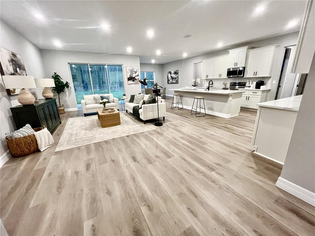 An open-concept living room and kitchen feature light wood flooring and white cabinetry — 6 BELLIS COURT, HOMOSASSA, FL