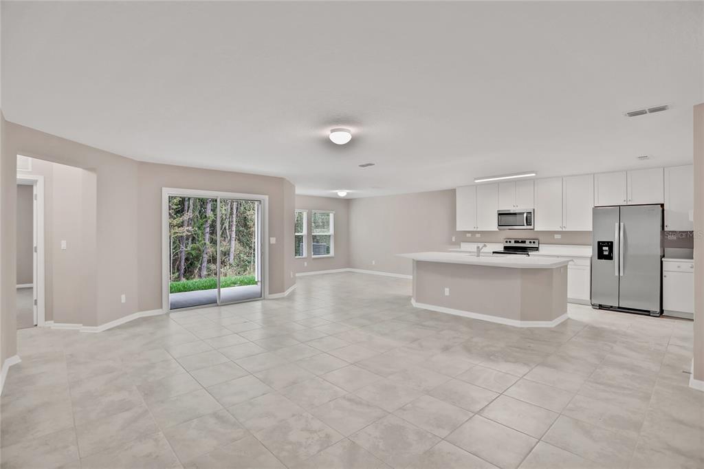 An open-concept kitchen and living area features white cabinetry, stainless steel appliances, and tile flooring — 2760 LAUREL FALLS DRIVE, GREEN COVE SPRINGS, FL