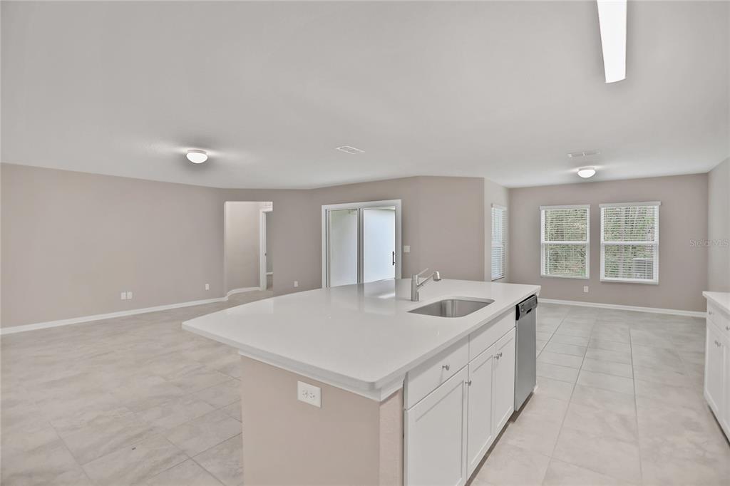 A kitchen island with a sink sits in an open-concept room with light-colored tile flooring — 2760 LAUREL FALLS DRIVE, GREEN COVE SPRINGS, FL
