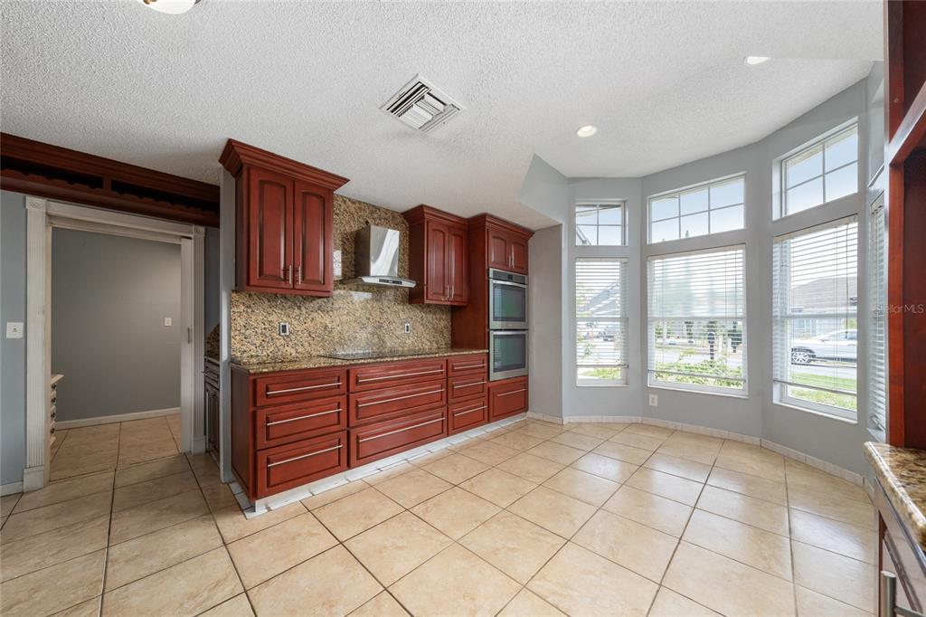 A kitchen with cherry wood cabinets, granite countertops, stainless steel appliances, and tiled flooring — 8810 KENSINGTON COURT, KISSIMMEE, FL