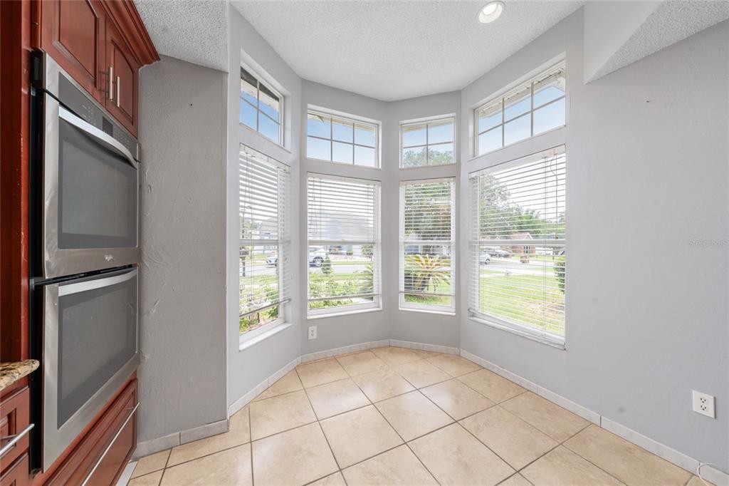 A kitchen features cherry wood cabinets, granite countertops, tile flooring, and a large bay window — 8810 KENSINGTON COURT, KISSIMMEE, FL