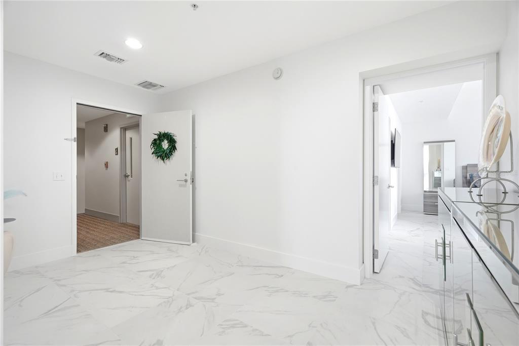A bright entryway features white marble-look tile flooring, two open doorways, and a green wreath — 175 1ST STREET S UNIT 1008, ST PETERSBURG, FL