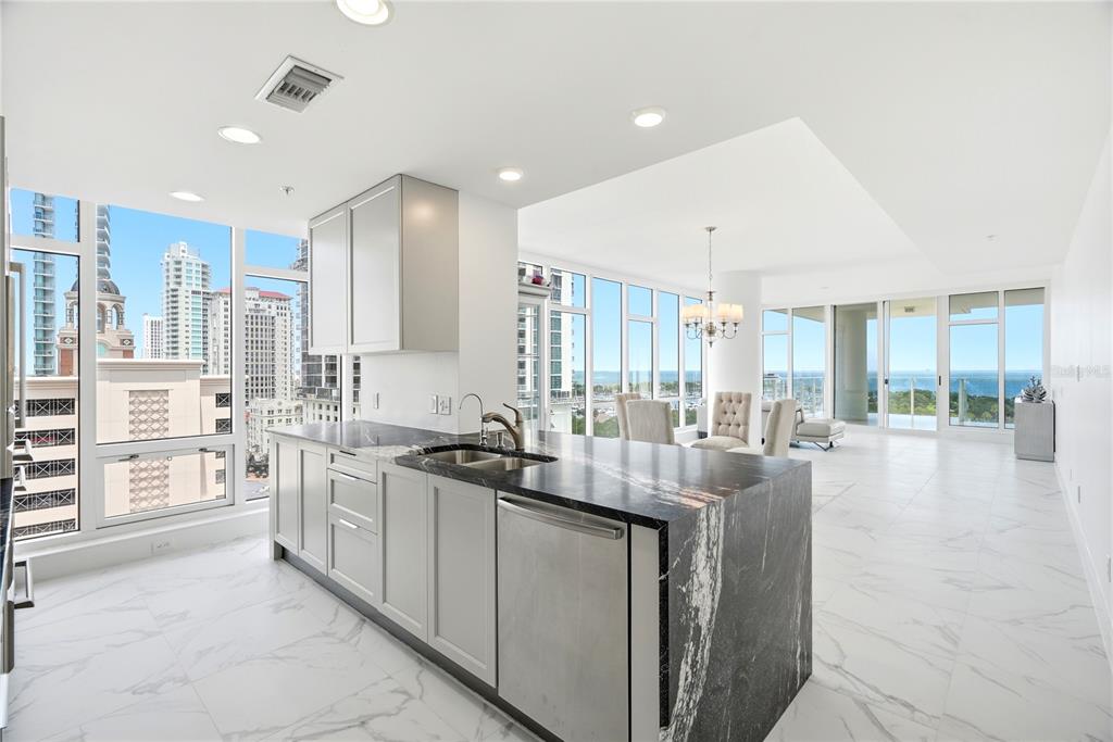 A modern kitchen with a black marble island overlooks a dining area and city skyline — 175 1ST STREET S UNIT 1008, ST PETERSBURG, FL