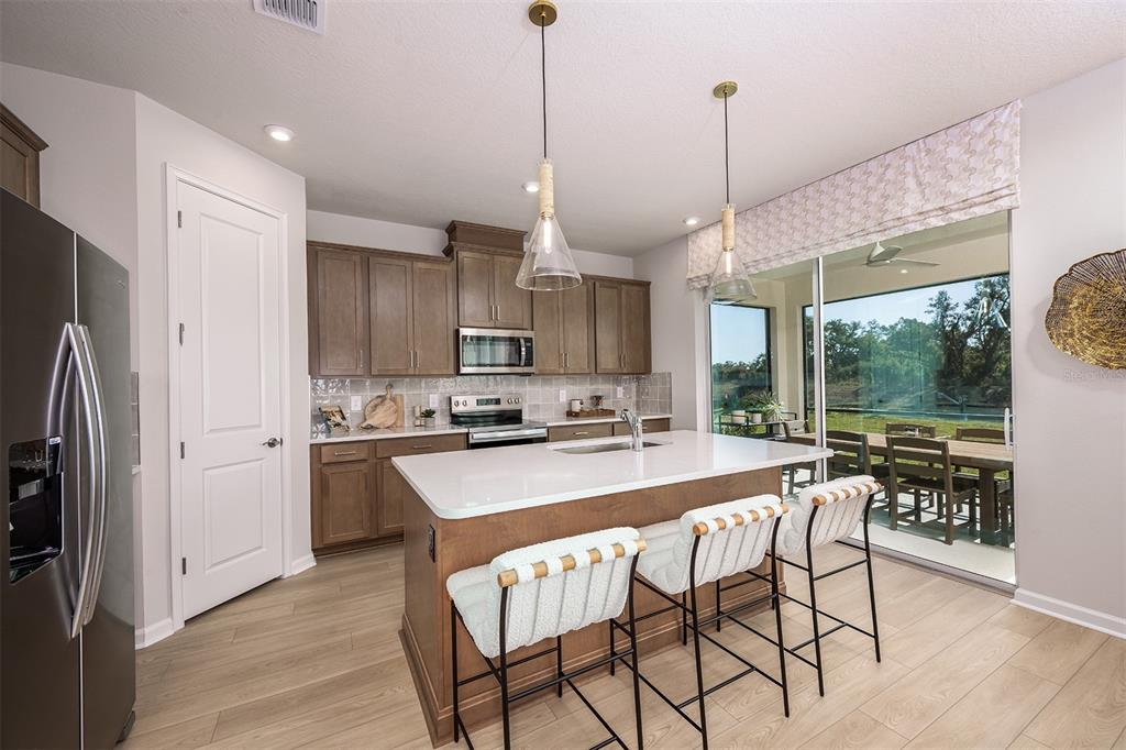 A modern kitchen features a central island with bar seating, wood cabinetry, and sliding glass doors — 1710 SOARING VIDA STREET, PALMETTO, FL