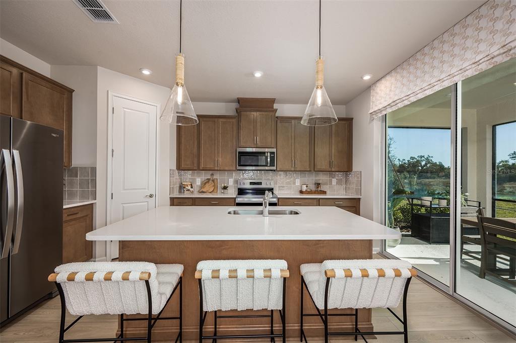 A kitchen with wood cabinets, a white quartz island, and sliding glass doors to a patio — 1710 SOARING VIDA STREET, PALMETTO, FL