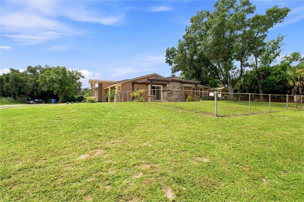 A single-story house with a stone chimney and pergola sits behind a chain-link fence — 9020 AUBURN WAY, TAMPA, FL