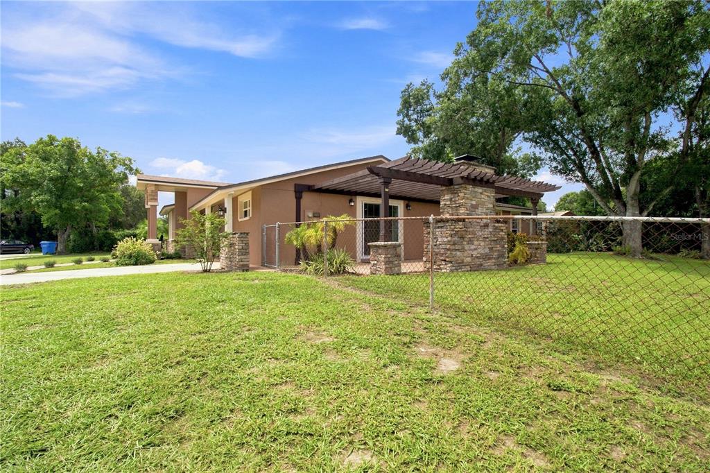 The exterior of a house features a stone chimney, a wooden pergola, and a chain-link fence — 9020 AUBURN WAY, TAMPA, FL