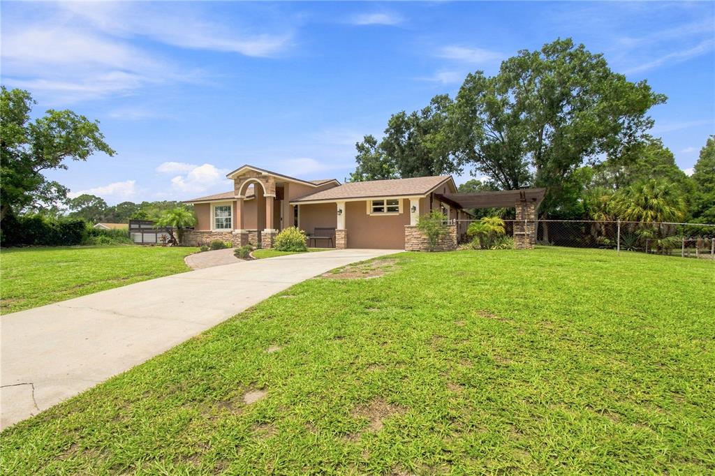 A single-story house with a tan exterior, stone accents, and a concrete driveway — 9020 AUBURN WAY, TAMPA, FL