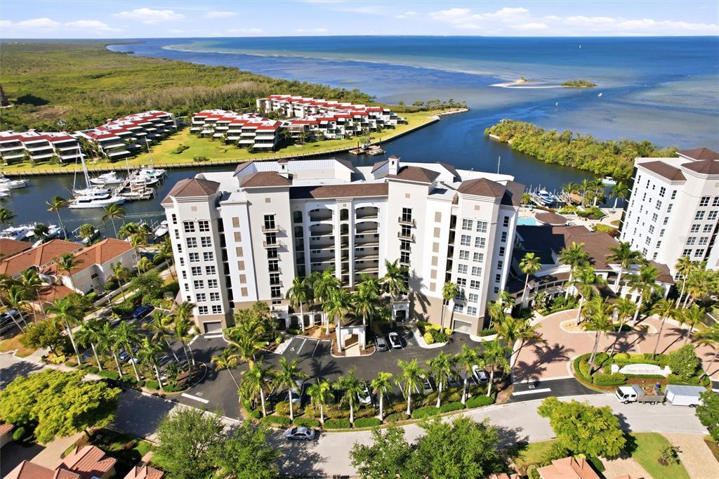 An aerial view shows a multi-story residential building surrounded by palm trees and a marina — 3313 SUNSET KEY CIRCLE UNIT 105, PUNTA GORDA, FL