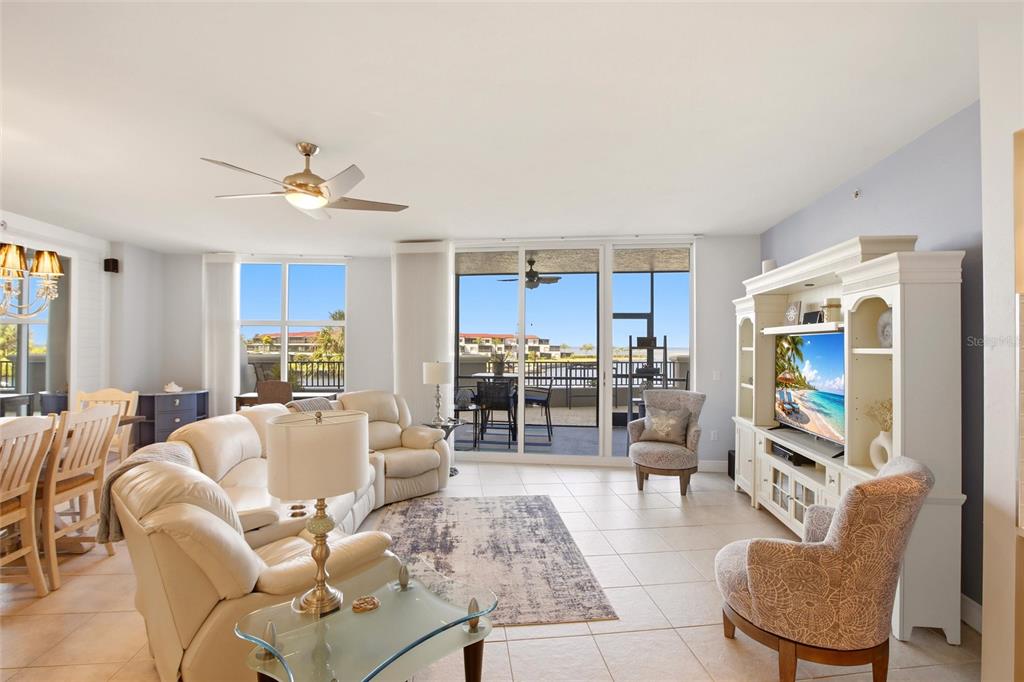 A bright living room features a white entertainment center, beige sectional sofa, and balcony access — 3313 SUNSET KEY CIRCLE UNIT 105, PUNTA GORDA, FL