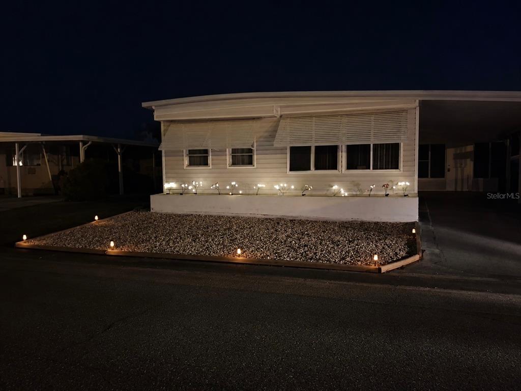 A single-story mobile home at night with illuminated landscaping and a gravel front yard — 47 KONO CIRCLE, LEESBURG, FL