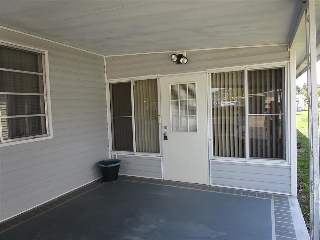 A covered patio with gray siding, a white door, and large windows with vertical blinds — 47 KONO CIRCLE, LEESBURG, FL