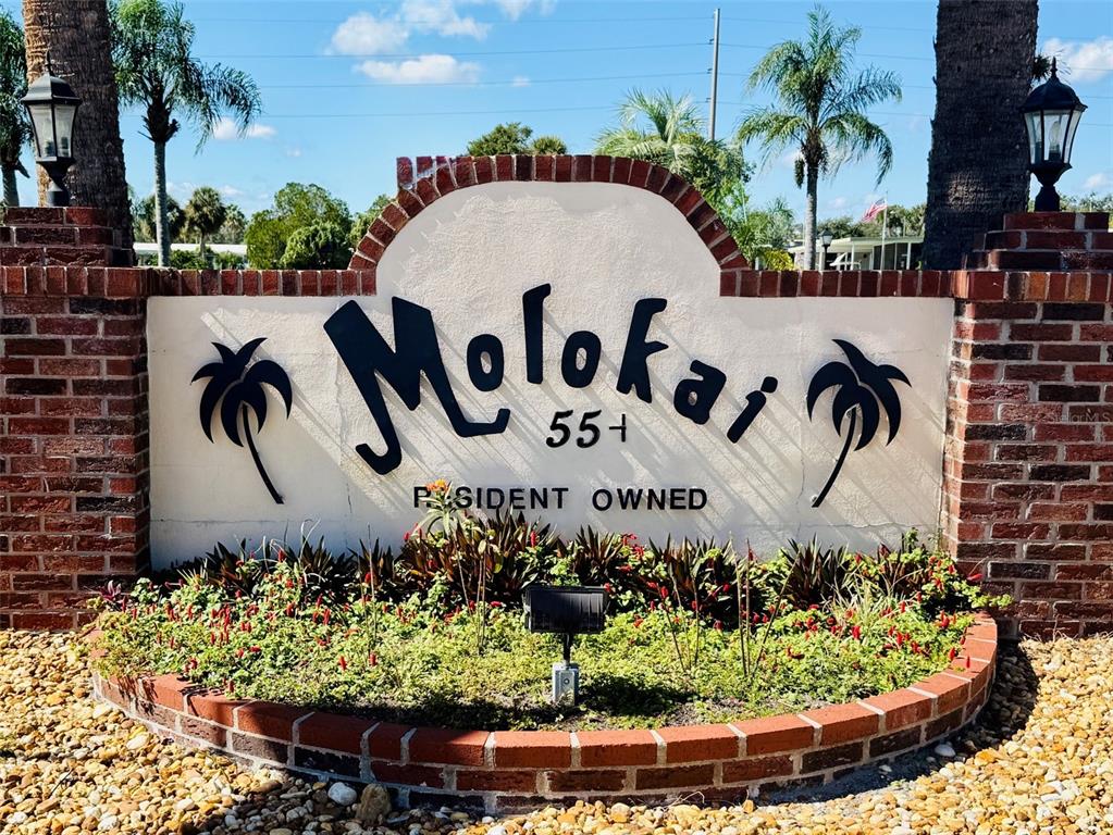 A brick-bordered sign for Molokai 55+ Resident Owned community sits in a landscaped garden — 47 KONO CIRCLE, LEESBURG, FL