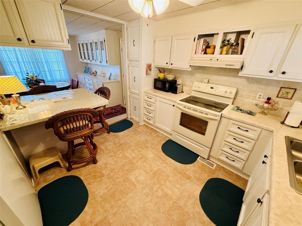 A kitchen with white cabinets, a white stove, and a dining area with wicker chairs — 47 KONO CIRCLE, LEESBURG, FL