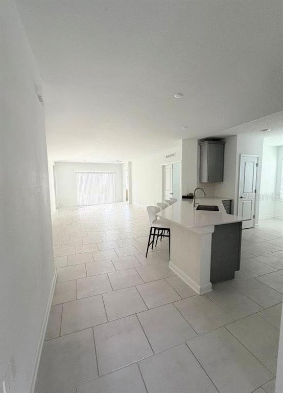 An open-concept kitchen with a white island and gray cabinets overlooks a tiled living area — 5692 STEPHENS ROAD, ST CLOUD, FL