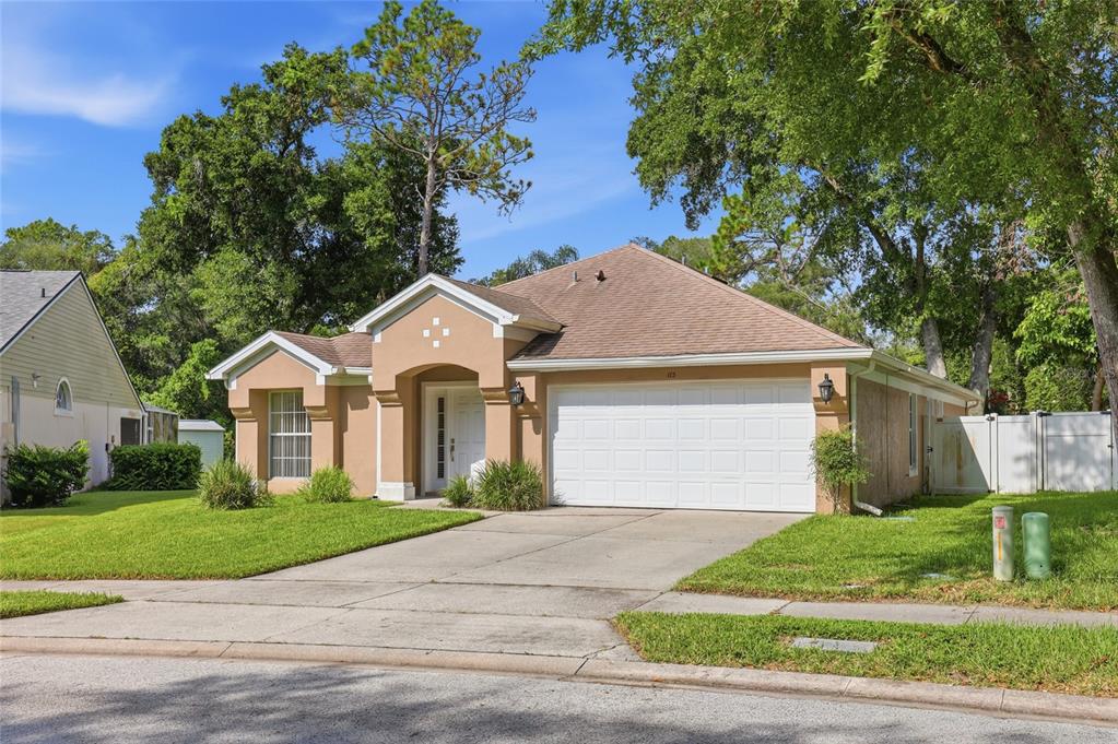 A tan single-story house with a two-car garage and a concrete driveway under a blue sky — 115 N WEATHERSFIELD AVENUE, ALTAMONTE SPRINGS, FL