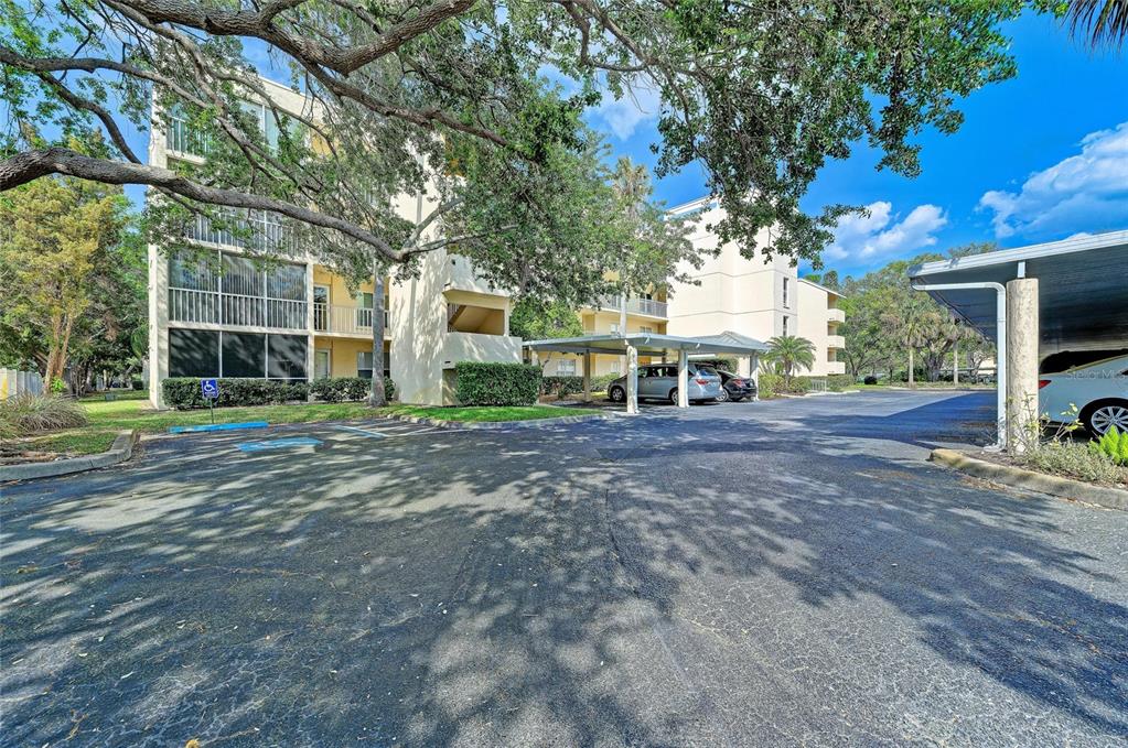A multi-story apartment building with covered parking spaces and mature trees in the foreground — 3980 IRONWOOD CIRCLE UNIT 206, BRADENTON, FL