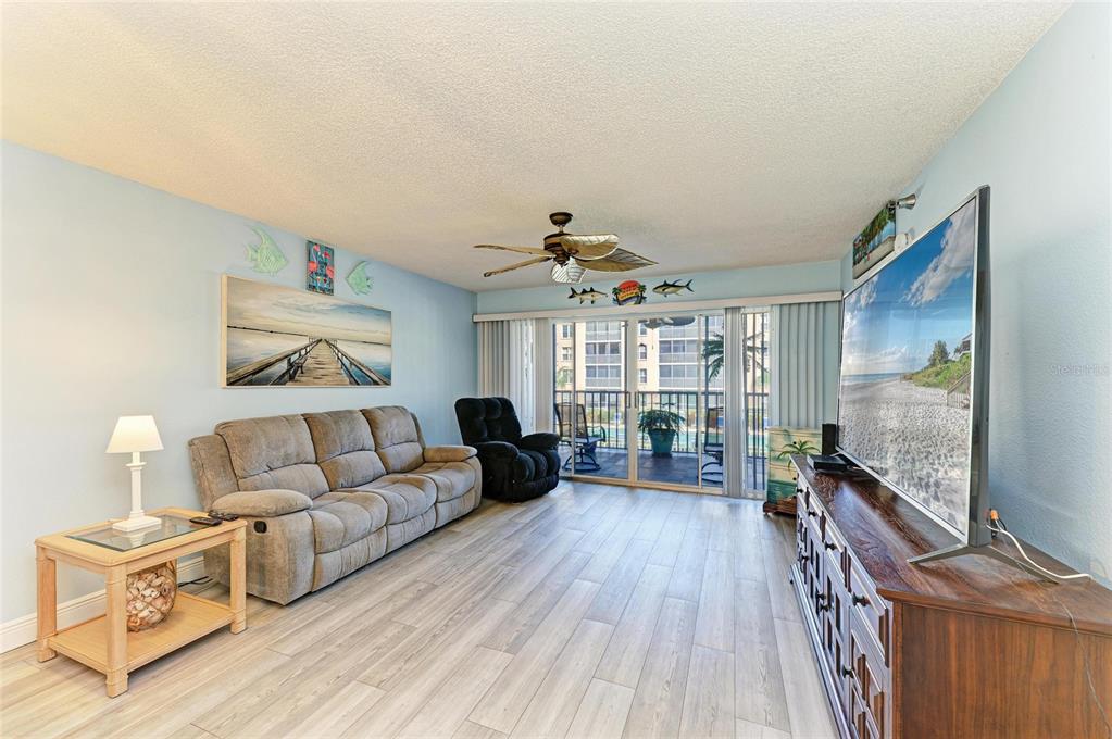 A living room features a gray sofa, a black recliner, a television, and sliding glass doors — 3980 IRONWOOD CIRCLE UNIT 206, BRADENTON, FL