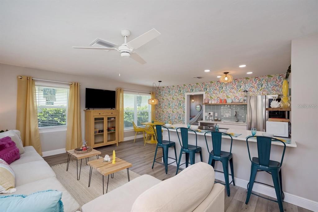An open-concept living room and kitchen featuring a floral accent wall and teal bar stools — 617 26TH STREET W, BRADENTON, FL