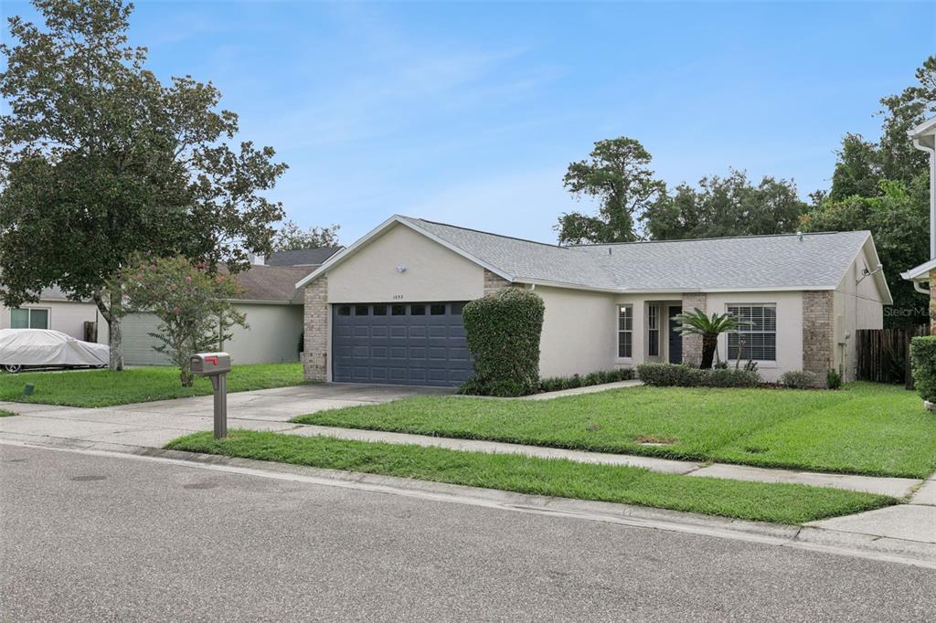 A single-story house with a gray garage door, beige stucco walls, and a grassy front yard — 1052 BRIELLE AVENUE, OVIEDO, FL