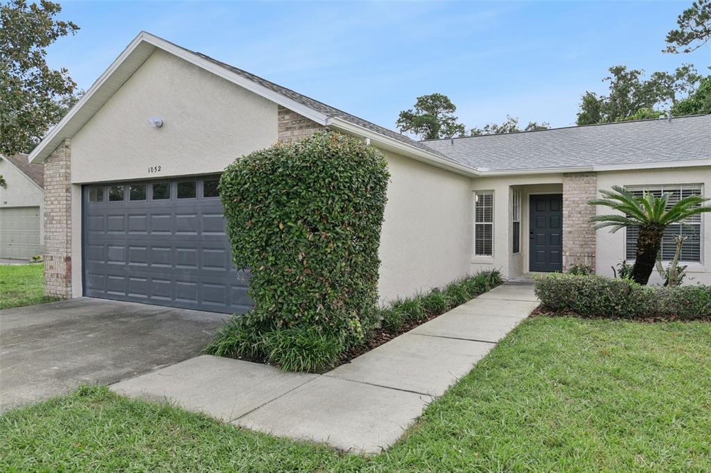 A single-story house with a gray garage door, beige stucco walls, and a concrete walkway — 1052 BRIELLE AVENUE, OVIEDO, FL