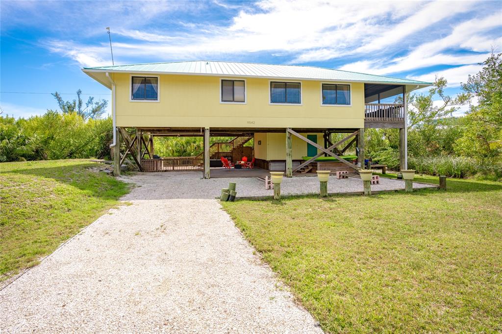 A yellow stilt house with a gravel driveway and a metal roof sits outdoors — 9542 RUM RUNNER ROAD, PLACIDA, FL