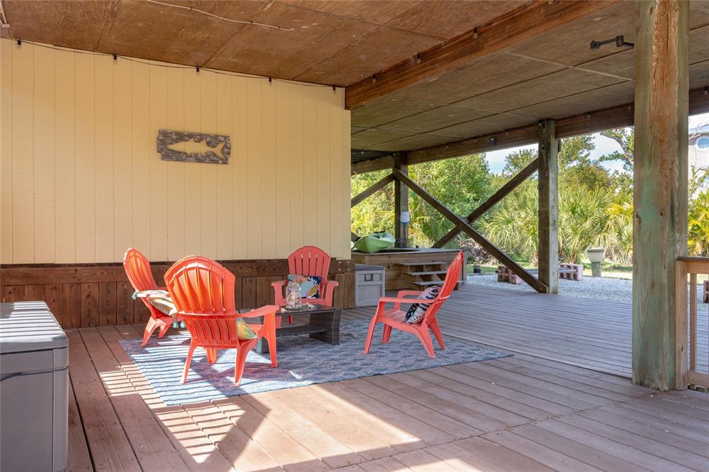 A covered wooden deck features orange Adirondack chairs arranged on a rug near a wall — 9542 RUM RUNNER ROAD, PLACIDA, FL