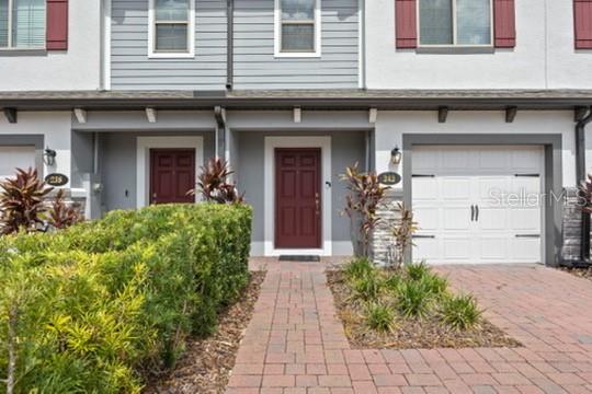 The exterior of a two-story townhouse features a brick walkway, red doors, and a garage — 242 CEDAR BARK LANE, SANFORD, FL