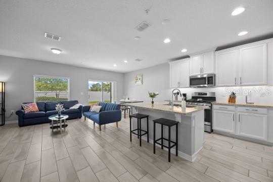 An open-concept kitchen and living area features white cabinetry, granite countertops, and tile flooring — 242 CEDAR BARK LANE, SANFORD, FL