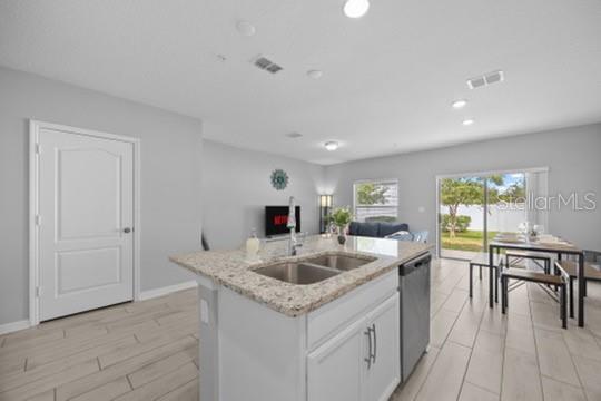 A kitchen island with a granite countertop and sink overlooks an open-concept living and dining area — 242 CEDAR BARK LANE, SANFORD, FL