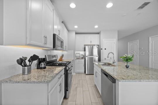 A modern kitchen features white cabinets, granite countertops, stainless steel appliances, and light wood-look flooring — 242 CEDAR BARK LANE, SANFORD, FL