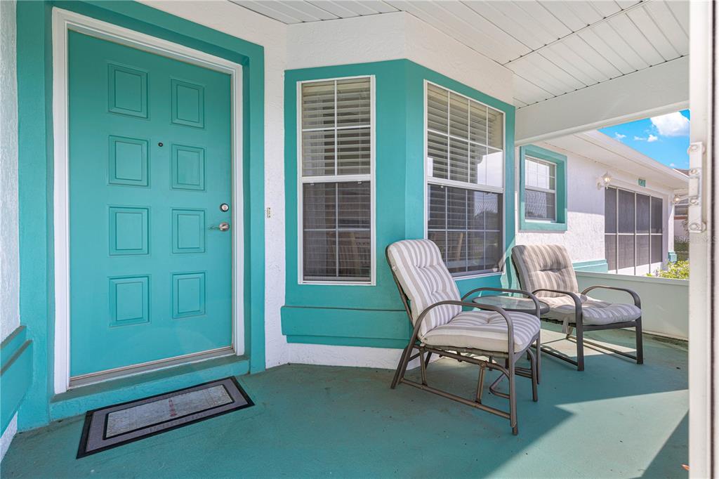 A covered front porch features a bright teal door, matching floor, and two outdoor chairs — 6201 SW 84TH PLACE, OCALA, FL