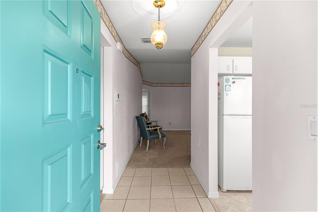 An entryway with a teal door, tiled floor, and a view into a carpeted living area — 6201 SW 84TH PLACE, OCALA, FL