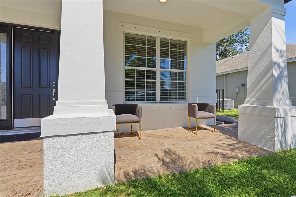 A covered front porch features tiled flooring, two gray chairs, and white structural columns — 8809 49TH AVENUE E, PALMETTO, FL
