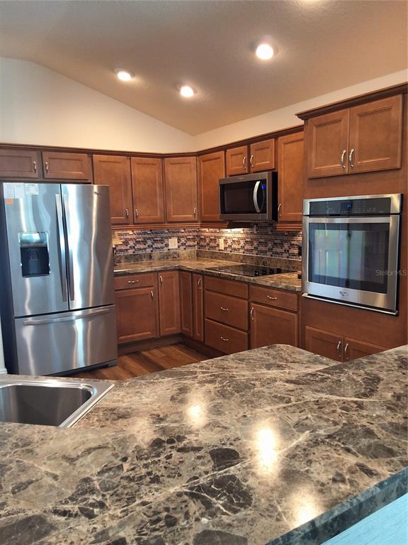 A kitchen features wood cabinets, stainless steel appliances, and dark granite countertops — 3526 CLUSTER COURT, THE VILLAGES, FL