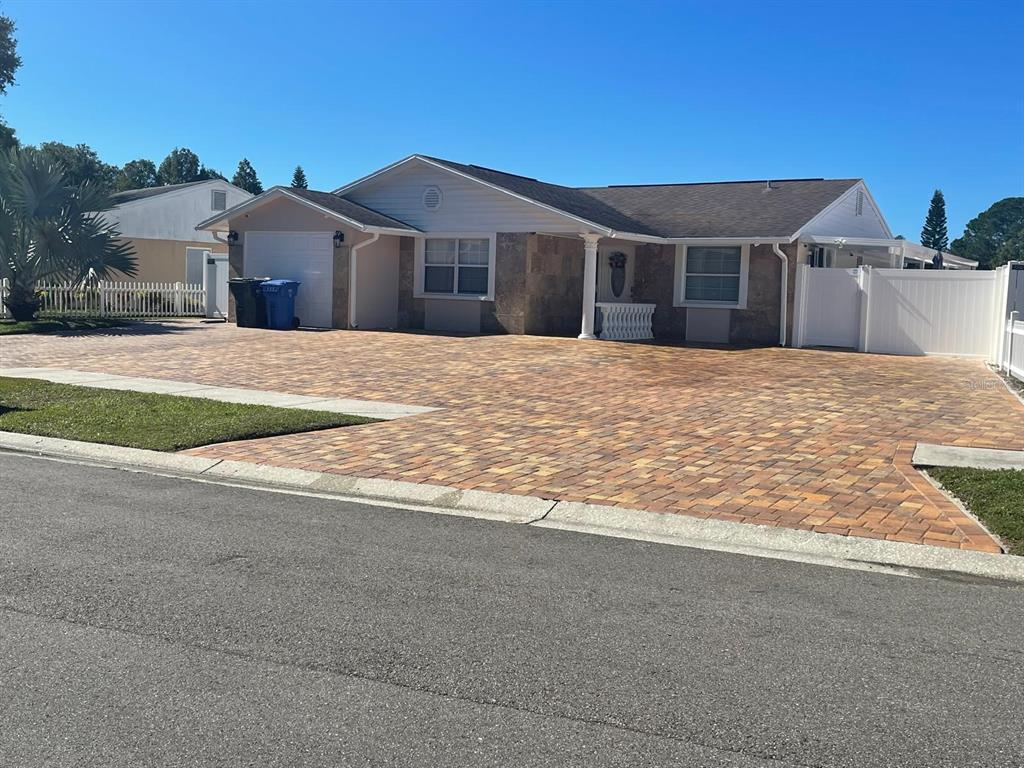 A single-story house features a large paver driveway, stone facade, and a white vinyl fence — 6423 MONTEREY BOULEVARD, TAMPA, FL