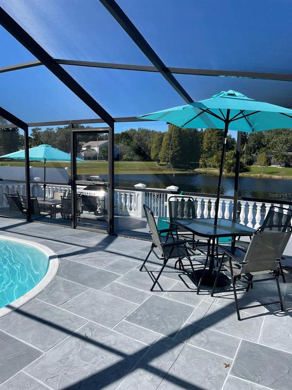 A screened-in pool patio features a dining set, umbrellas, and views of a lake — 6423 MONTEREY BOULEVARD, TAMPA, FL